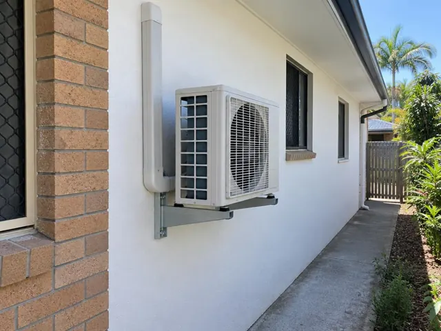 Wall-mounted air conditioner outdoor unit beside a brick and rendered house wall in Reedy Creek